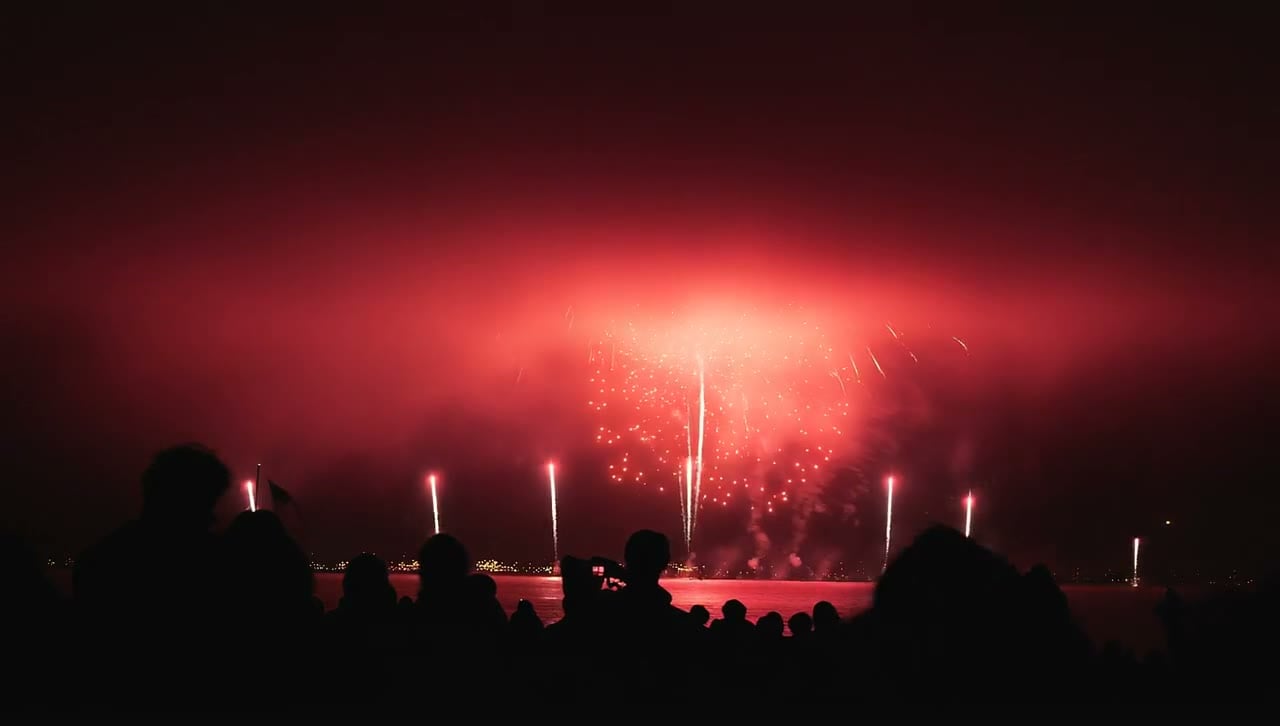 Red fireworks over a crowd at a lake